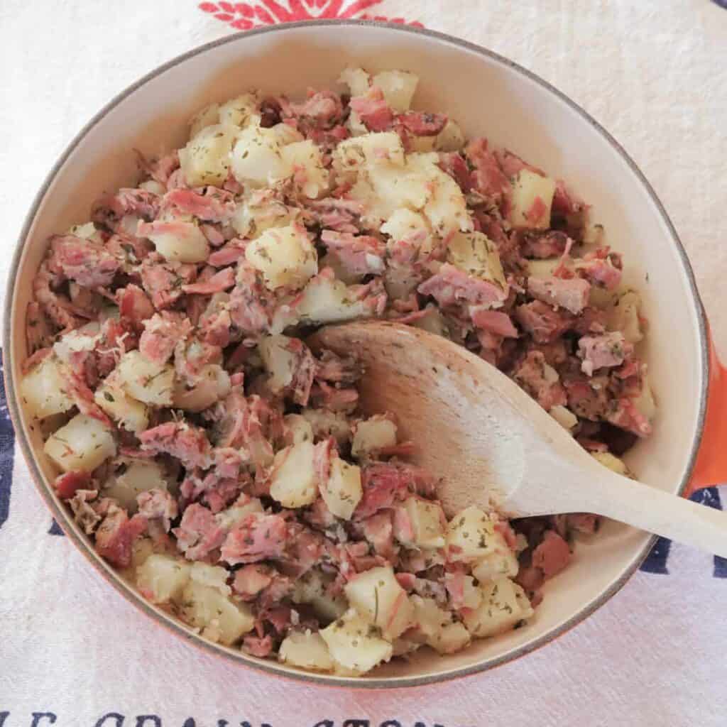 Skillet of corned beef hash and a wooden spoon