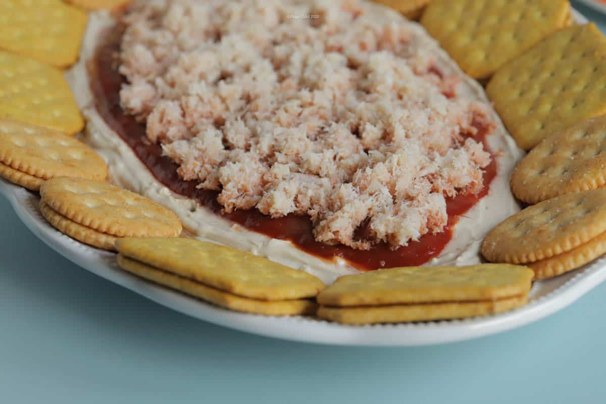 Close up of crabmeat sprinkled on top of crab dip and surrounded by crackers