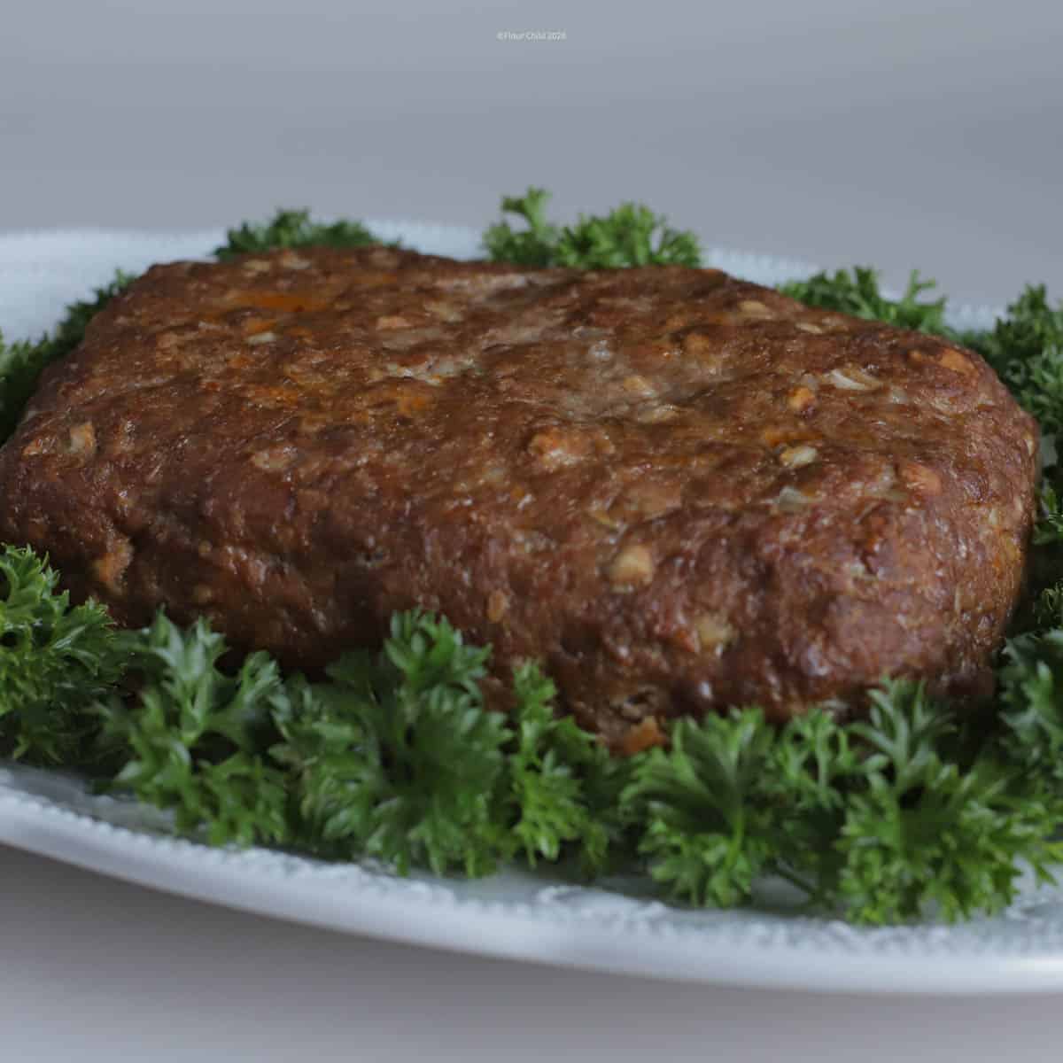 Delicious meatloaf with tomato and onion on platter set on a bed of parsley