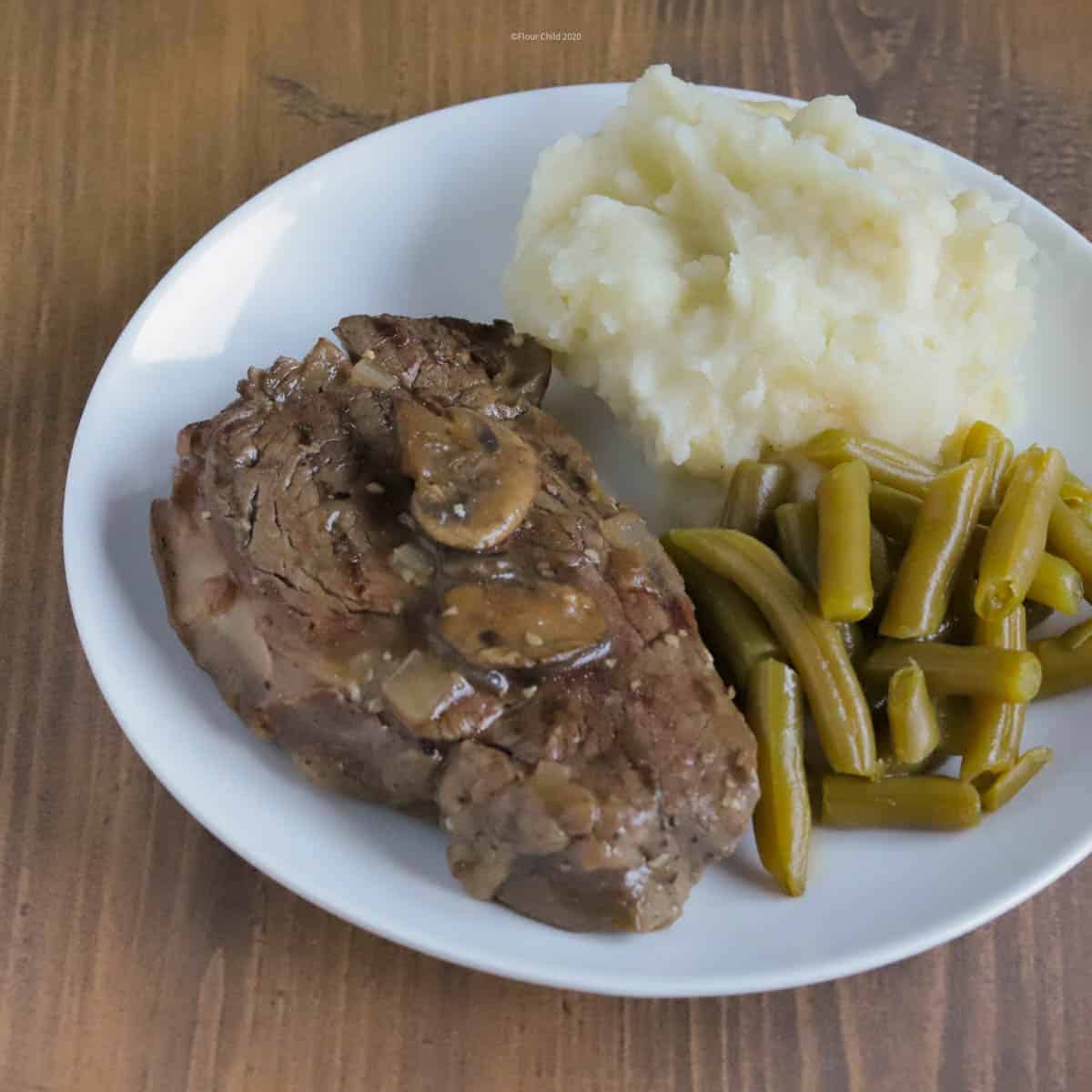 Photo of filet mignon in wine sauce on a dinner plate with mashed potatoes and green beans