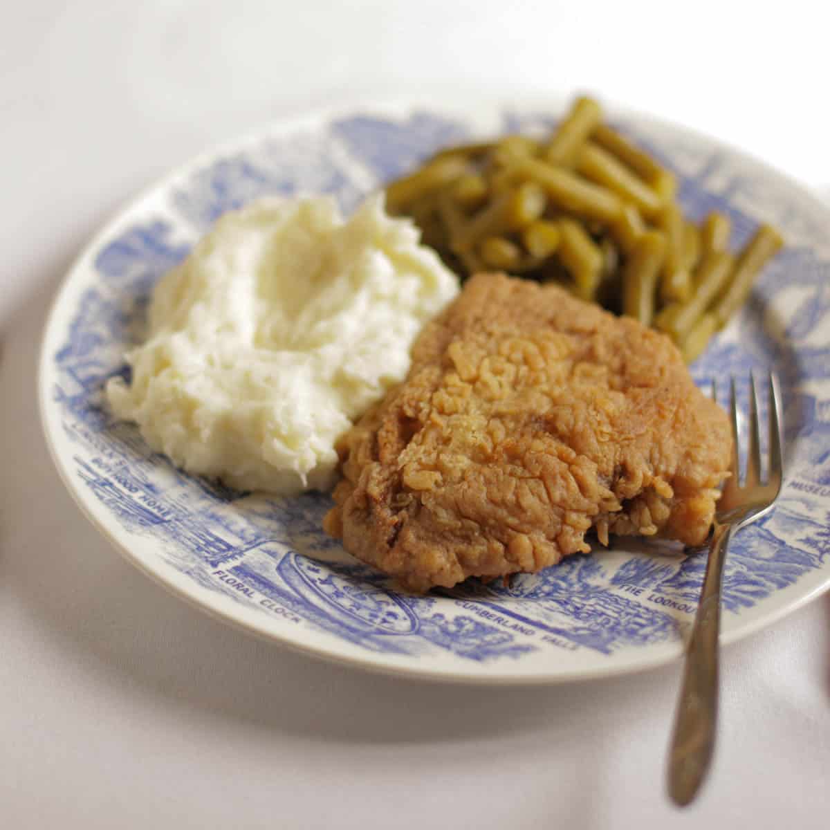 Chicken fried steak on a plate next to mashed potatoes and green beans.