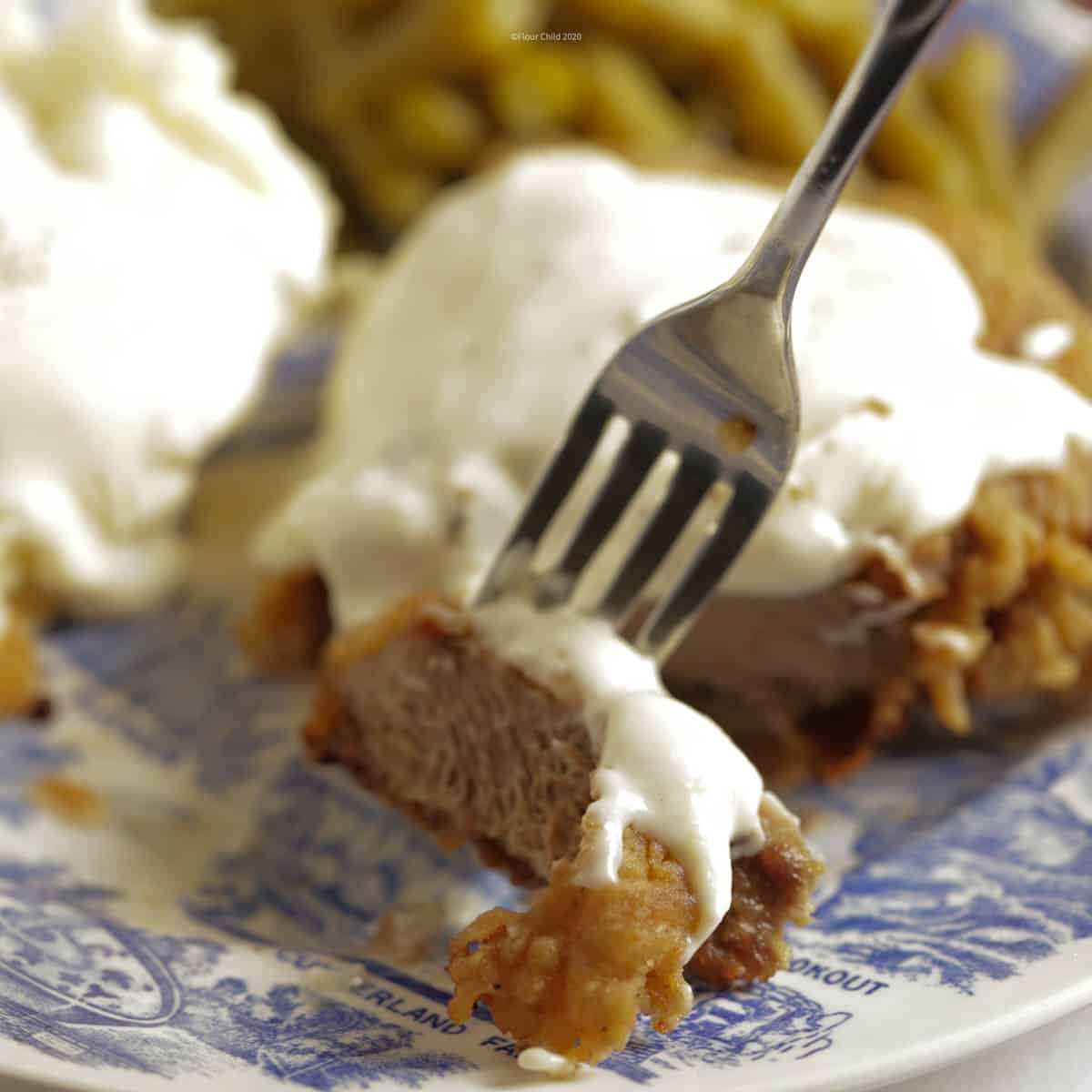 A close up of a piece of chicken fried steak on a fork with white gravy on top