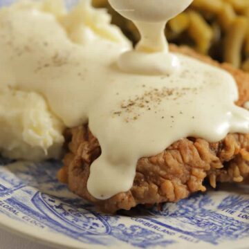 A close up of chicken fried steak on a plate with white pepper gravy being poured over the top