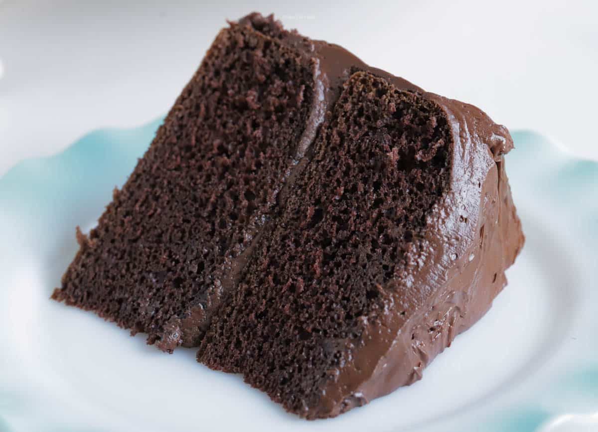 A slice of chocolate cake on a plate covered in chocolate buttercream frosting