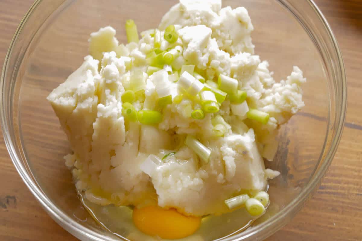 Leftover mashed potatoes, green onion and egg in a mixing bowl.