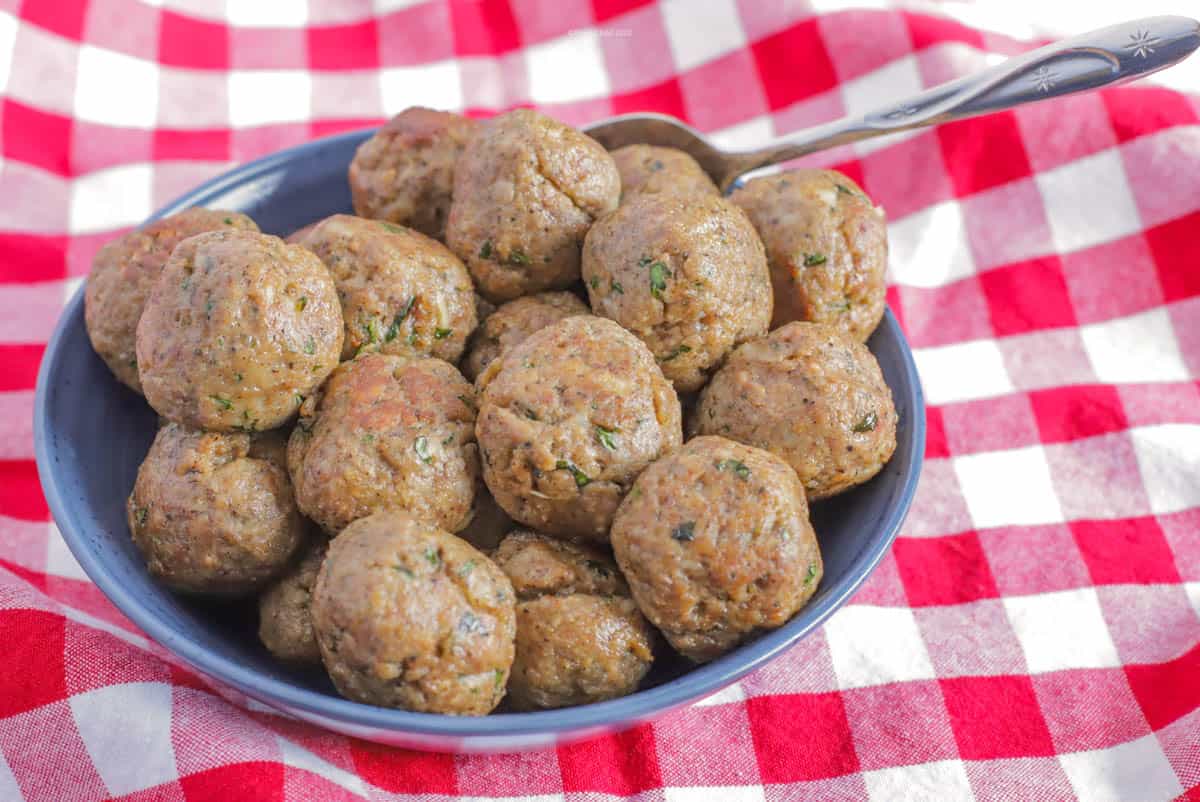 Two dozen meatballs piled into a blue bowl on top of a red checkerboard tablecloth