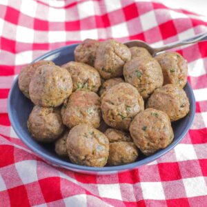Meatballs piled into a blue bowl on top of a red checkered tablecloth