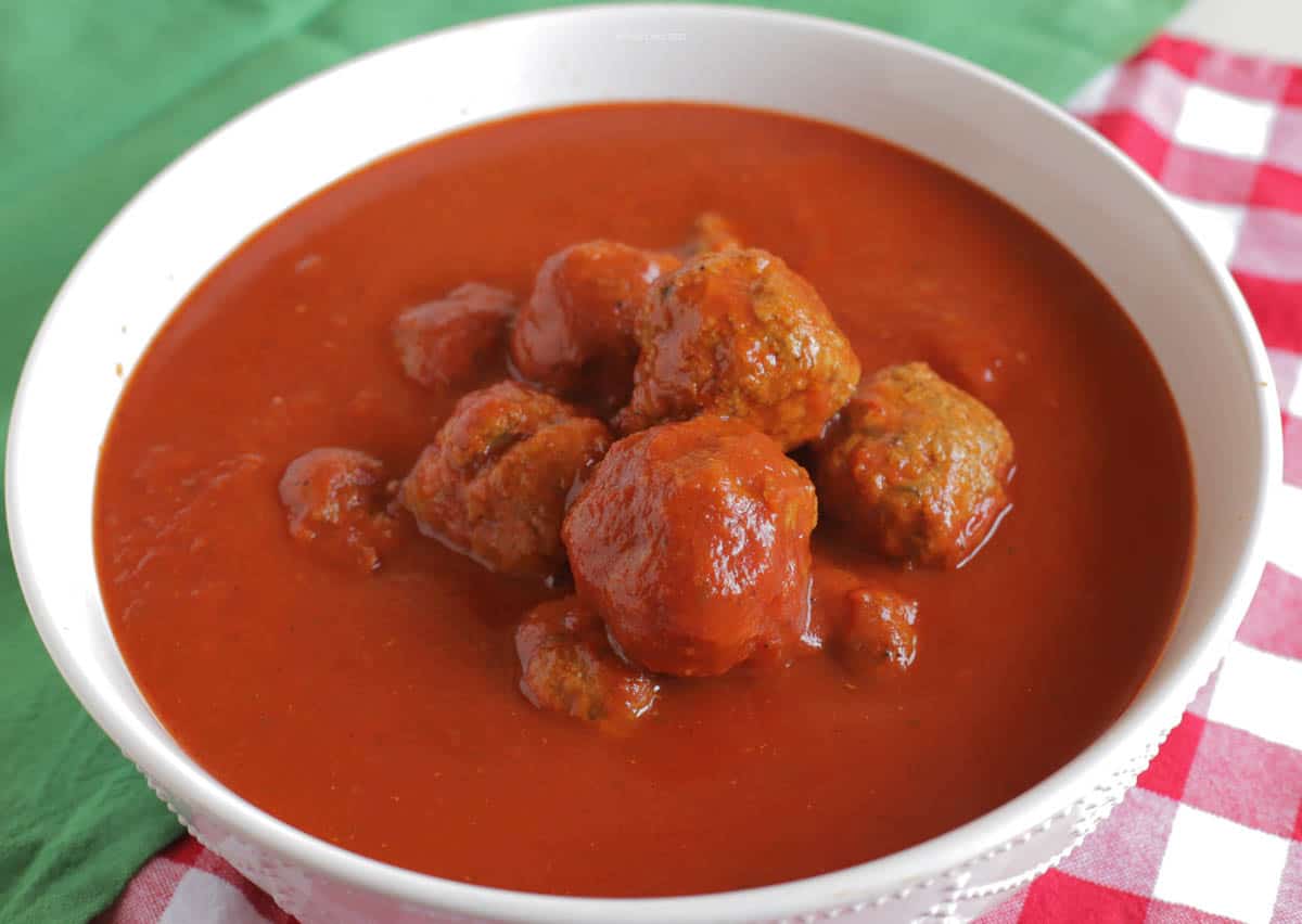 A pile of meatballs in a white bowl, topped with Italian red sauce