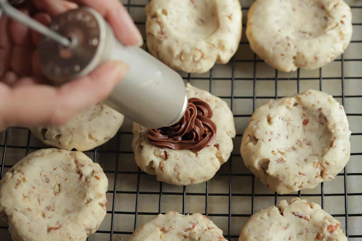 Chocolate frosting being piped onto a pecan cookie using a 1950's vintage dessert decorator