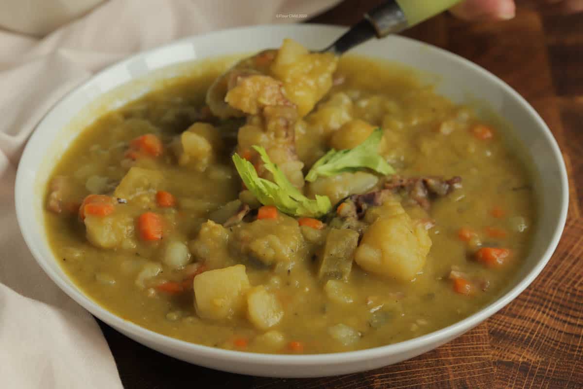 Bowl of split pea and ham soup with a celery leaf on top