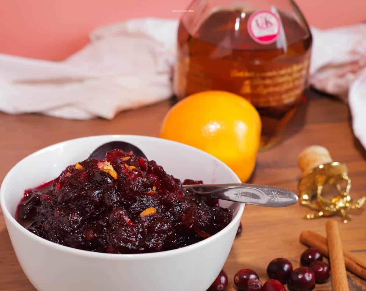 Cranberry sauce in a white bowl with an orange and bourbon in the background.