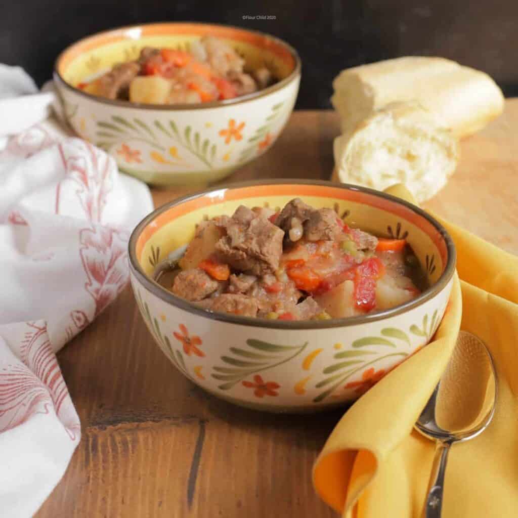 Two bowls of beef burgundy stew with a loaf of French bread sitting on a table