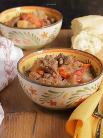 Two bowls of beef burgundy stew with a loaf of French bread sitting on a table