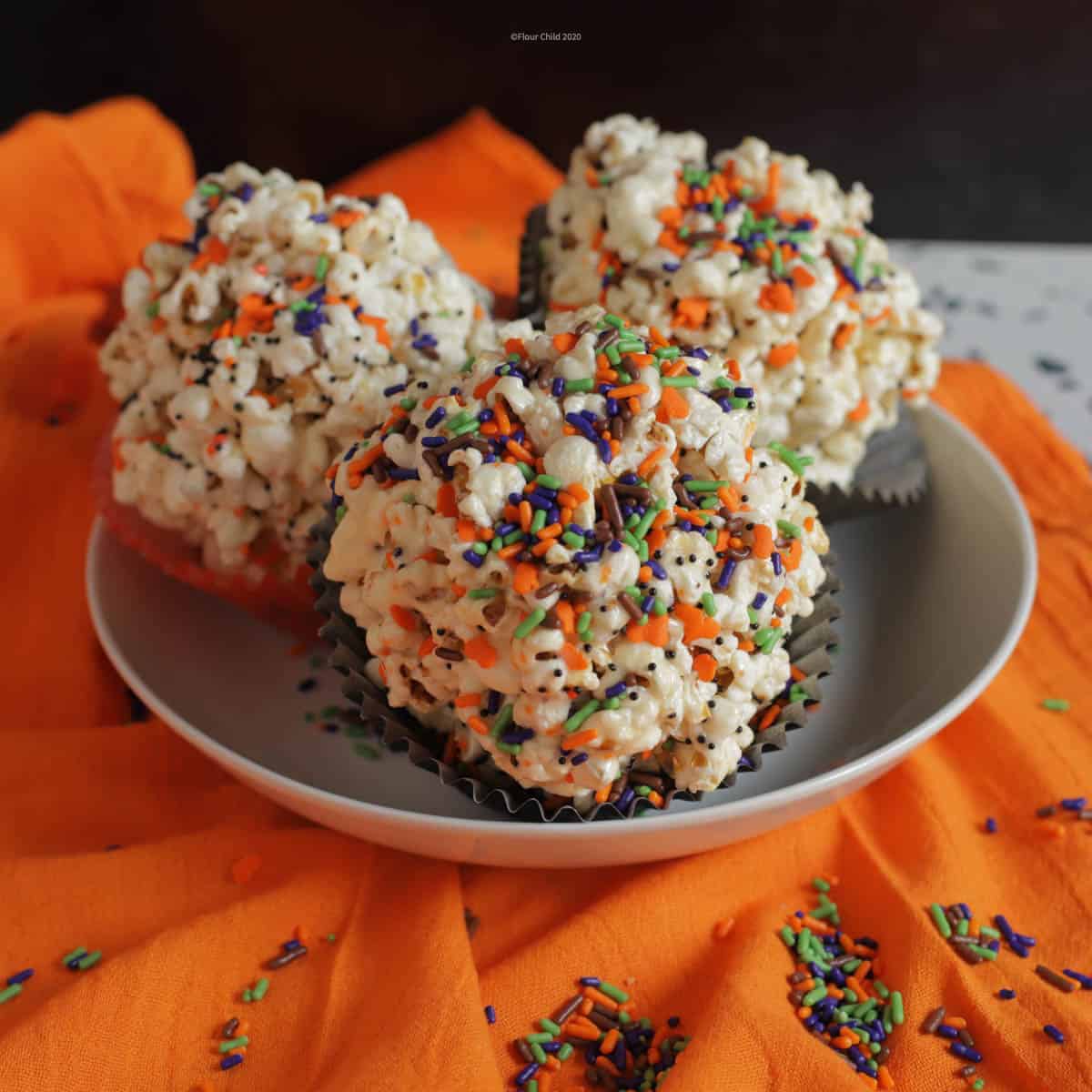 Three popcorn balls in a bowl with orange, green, black and purple candy sprinkles over them