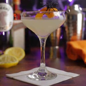 Cocktail served in a coupe glass with ingredients bottles blurred in the background