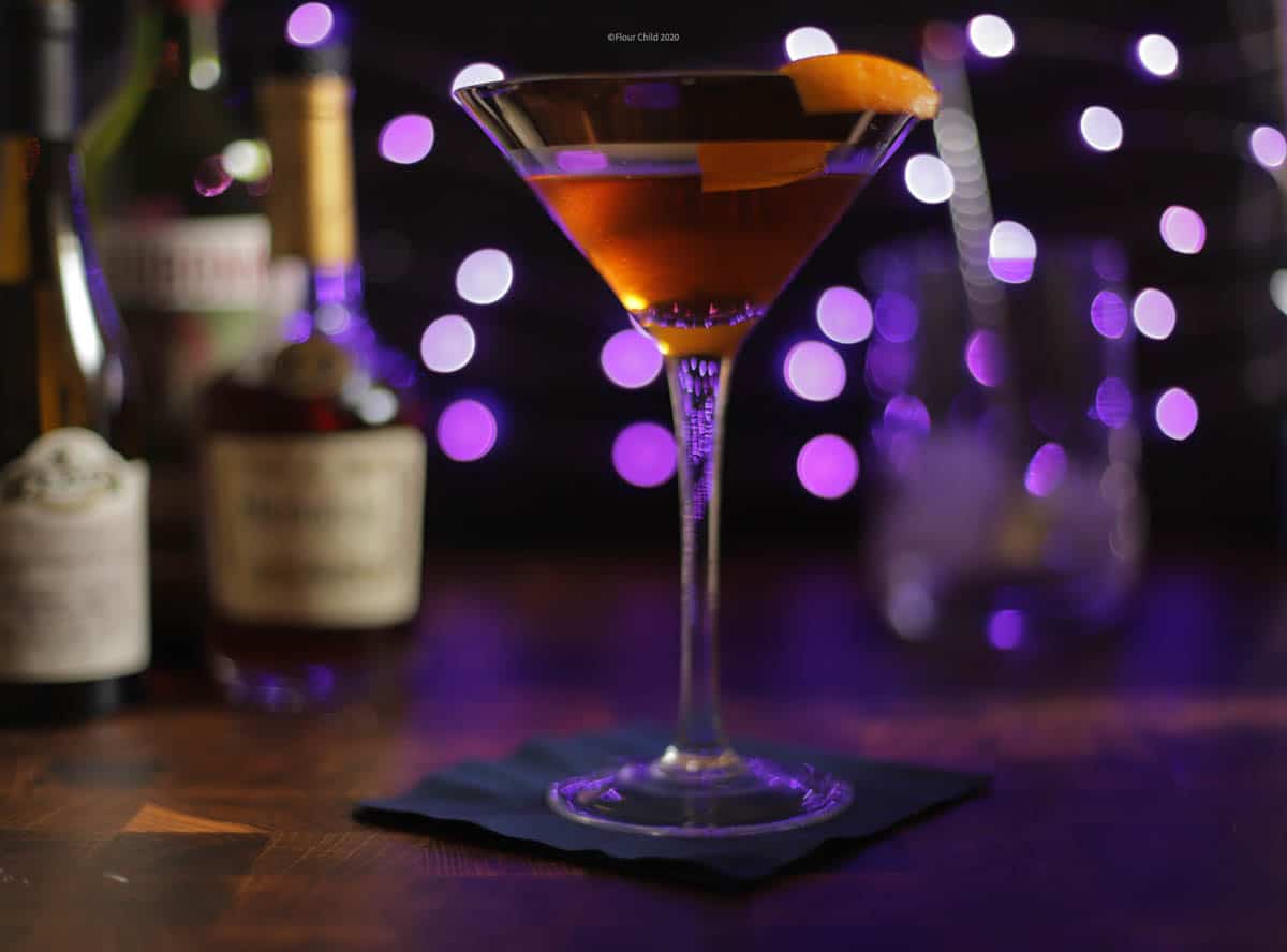 Corpse Reviver cocktail in a cocktail glass with an orange twist on a purple background.