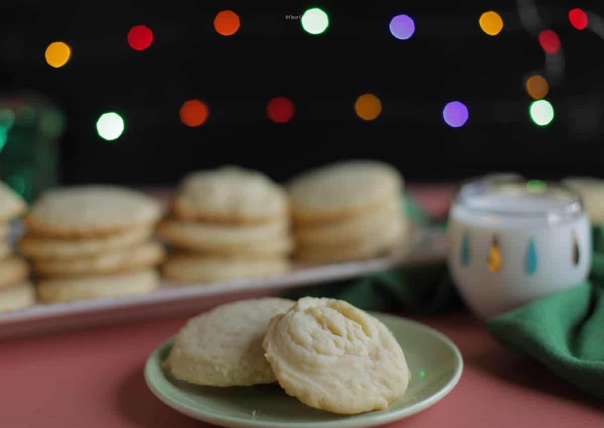 Two butter cookies on a green plate, with a tray of butter cookies behind it.