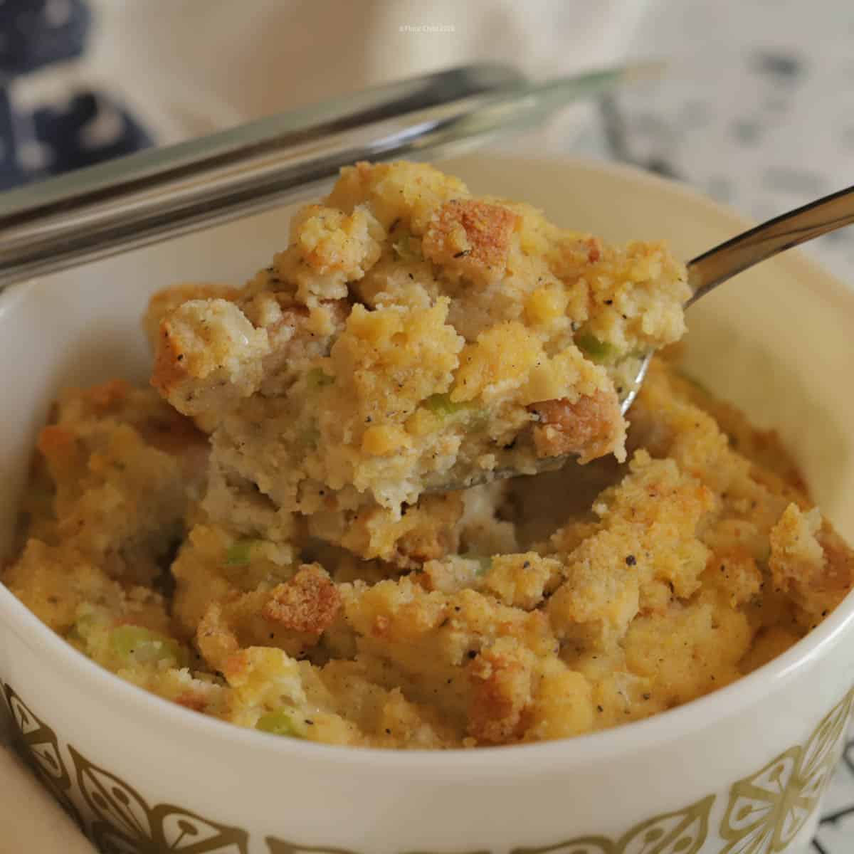 Cornbread stuffing in a white casserole dish with a spoonful being lifted out.