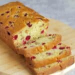 A loaf of cranberry orange quick bread on a cutting board with 3 slices cut off