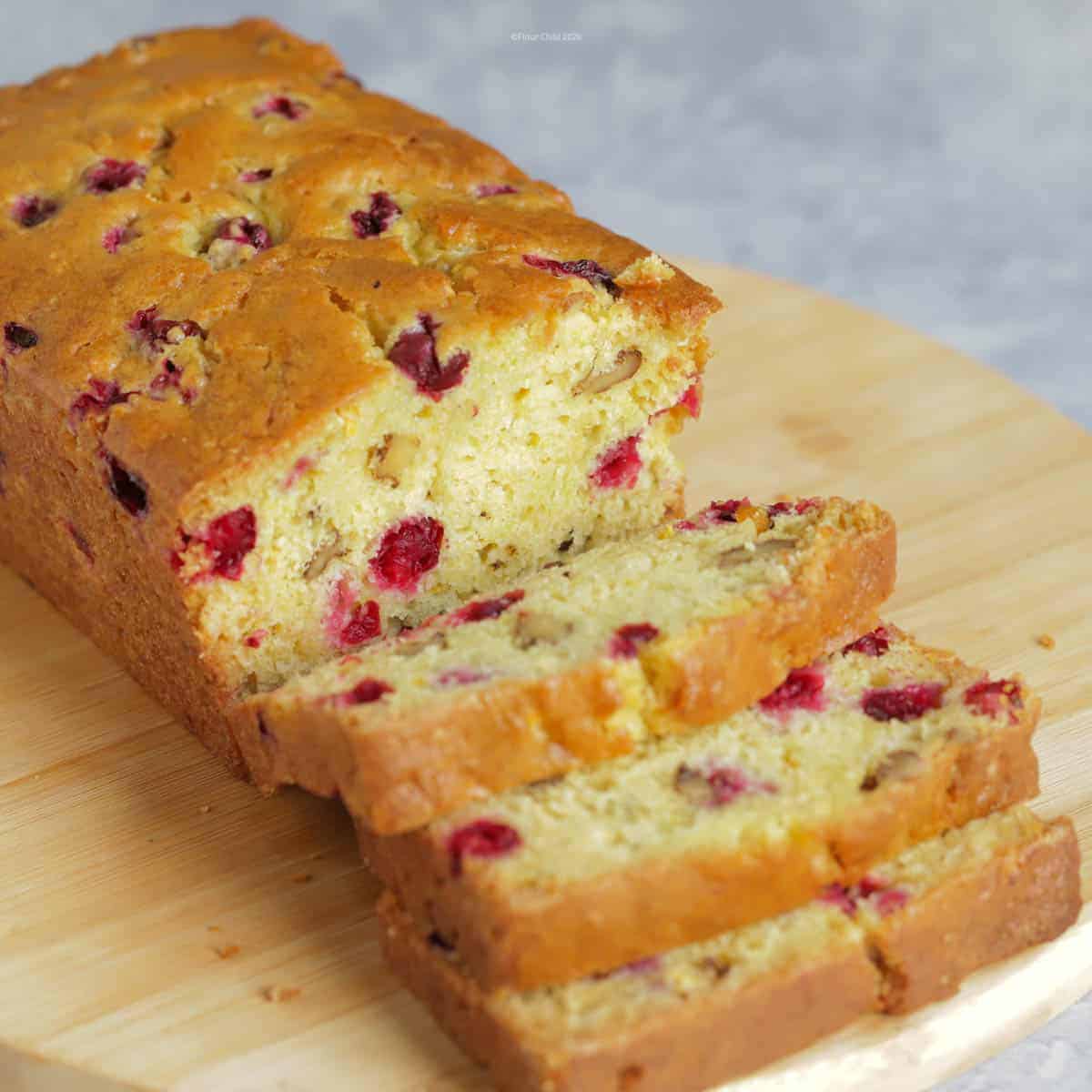 A loaf of cranberry orange quick bread on a cutting board with 3 slices cut off