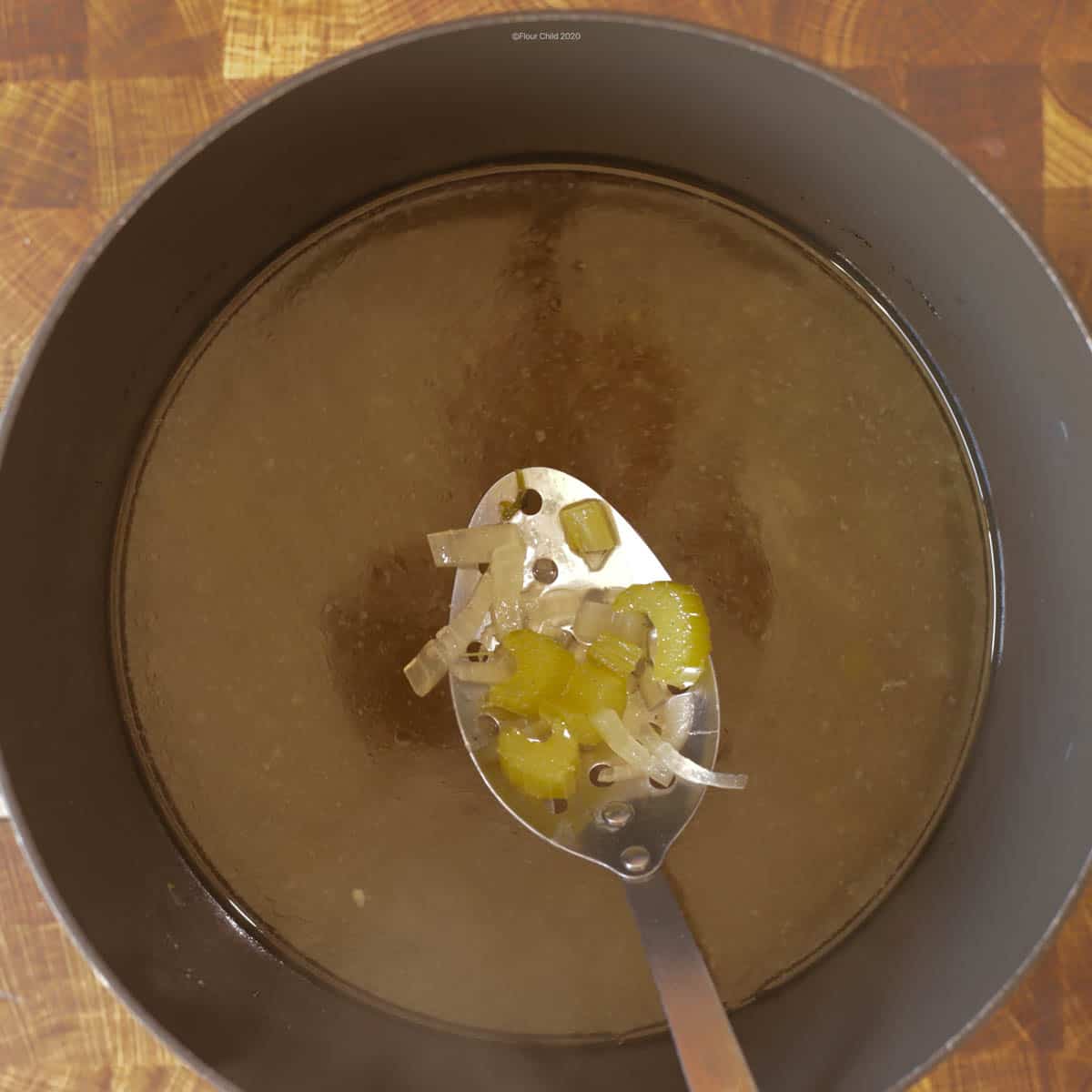 Pot of cooked chicken stock, with spoon lifting up onions, celery, & chicken