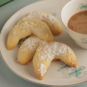 dessert plate with 3 crescent cookies next to a cup of coffee