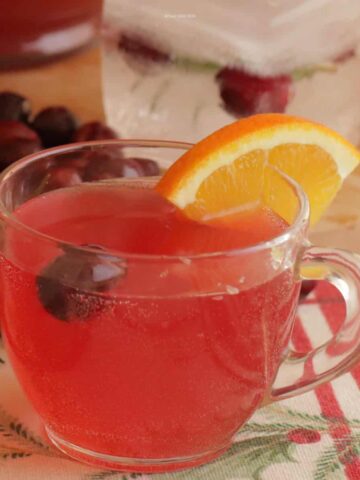 A punch glass filled with holiday punch and garnished with a sliced orange and cranberry.