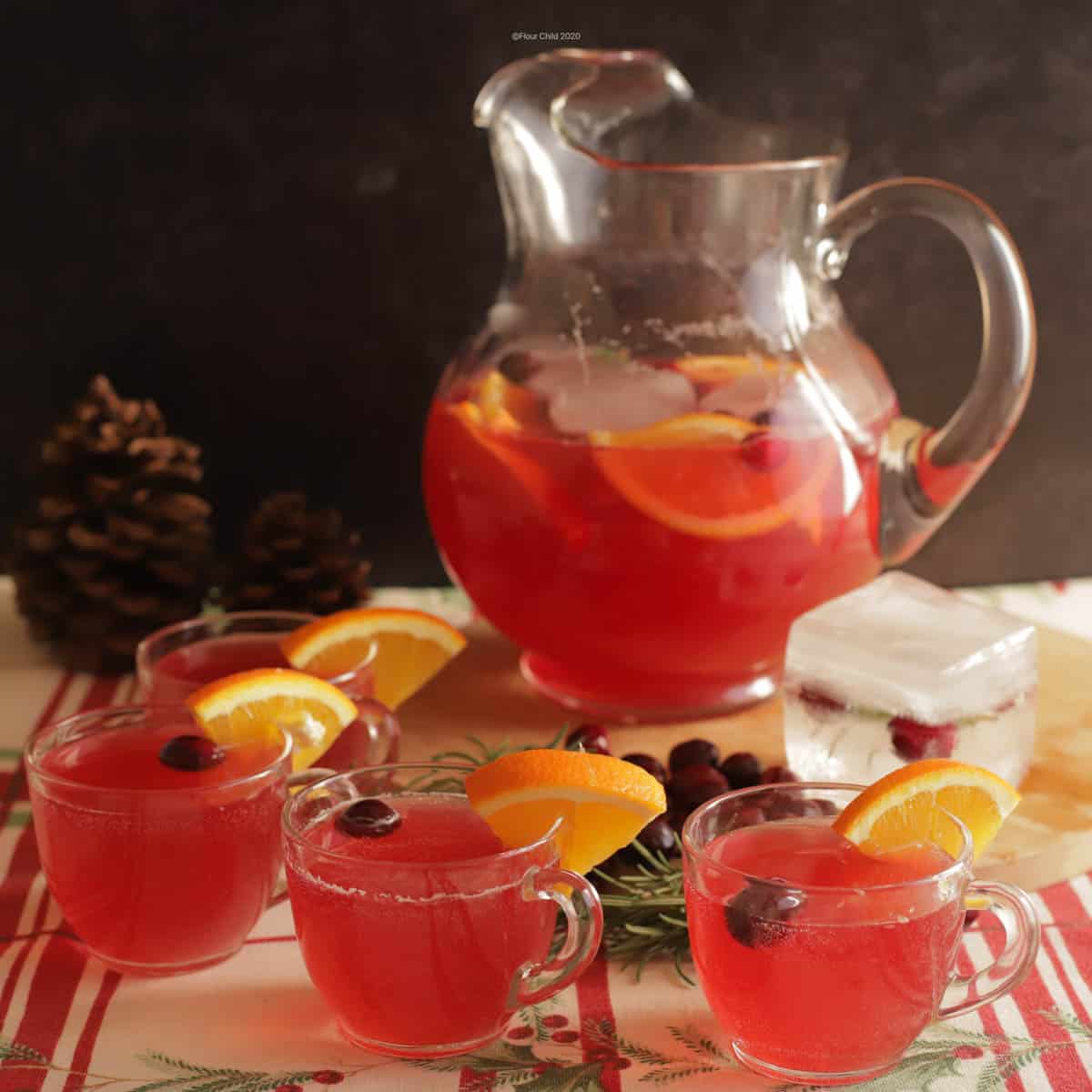 A pitcher of pink non alcoholic holiday punch with slices of orange and cranberries inside, with