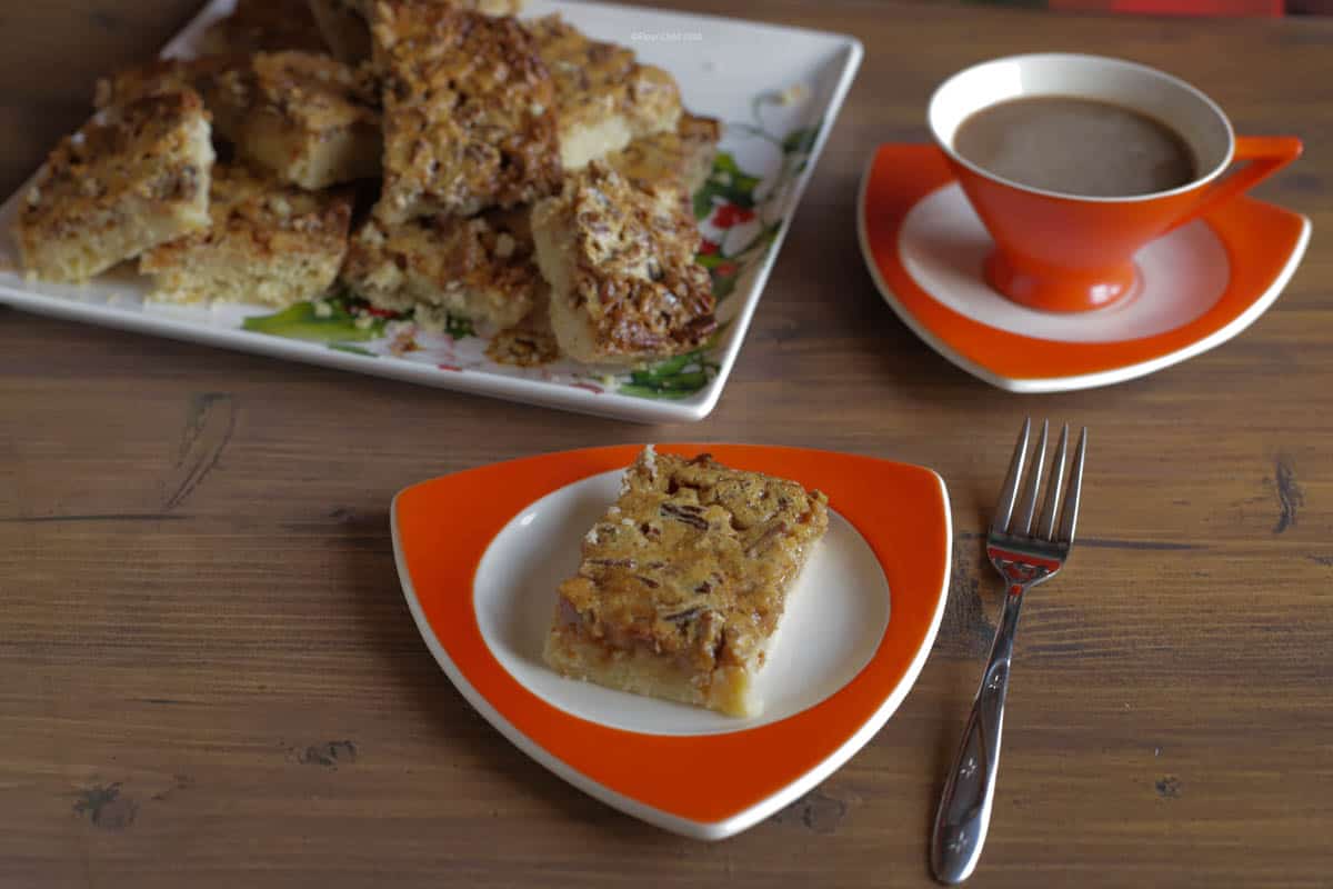 Three pecan pie bars stacked on top of each other, sitting on a small dessert plate