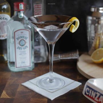 A Vesper Martini in a chilled cocktail glass with bottles and lemons in the background