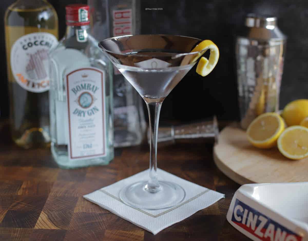 A Vesper Martini in a chilled cocktail glass with bottles and lemons in the background