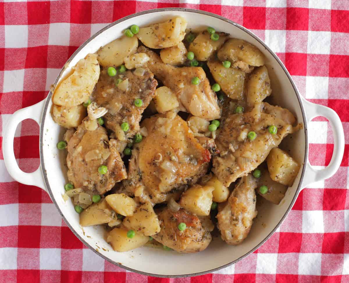 A white serving dish filled with chicken vesuvio sitting on a red checkered tablecloth