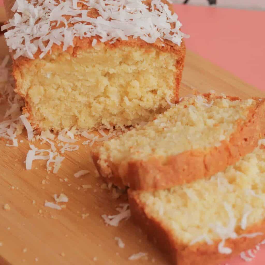 Two slices of coconut poundcake in front of the whole poundcake, with coconut sprinkled on top