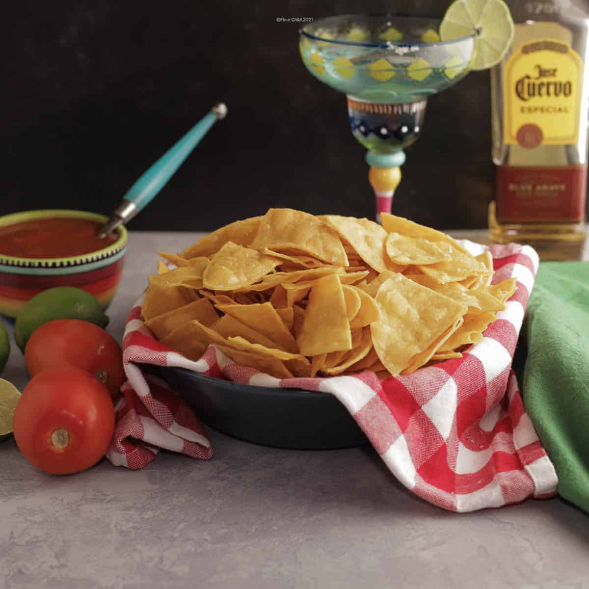 Basket of corn tortilla chips next to a bowl of salsa and a margarita