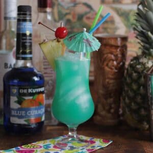 A Blue Hawaii cocktail in a hurricane glass with fruit and umbrella.