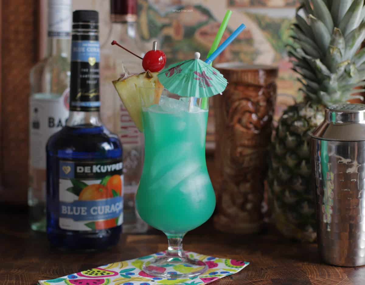 A Blue Hawaii cocktail in a hurricane glass with fruit and umbrella