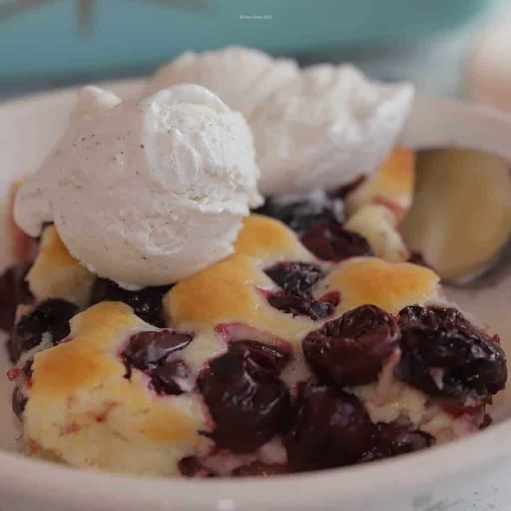 Cherry cobbler in a white bowl with two scoops of vanilla ice cream on top