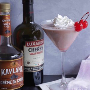 A frozen Pink Squirrel cocktail with two cherries and the bottles of liquor required.