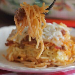 Fork scooping some spaghetti from a slice of baked spaghetti on a plate.