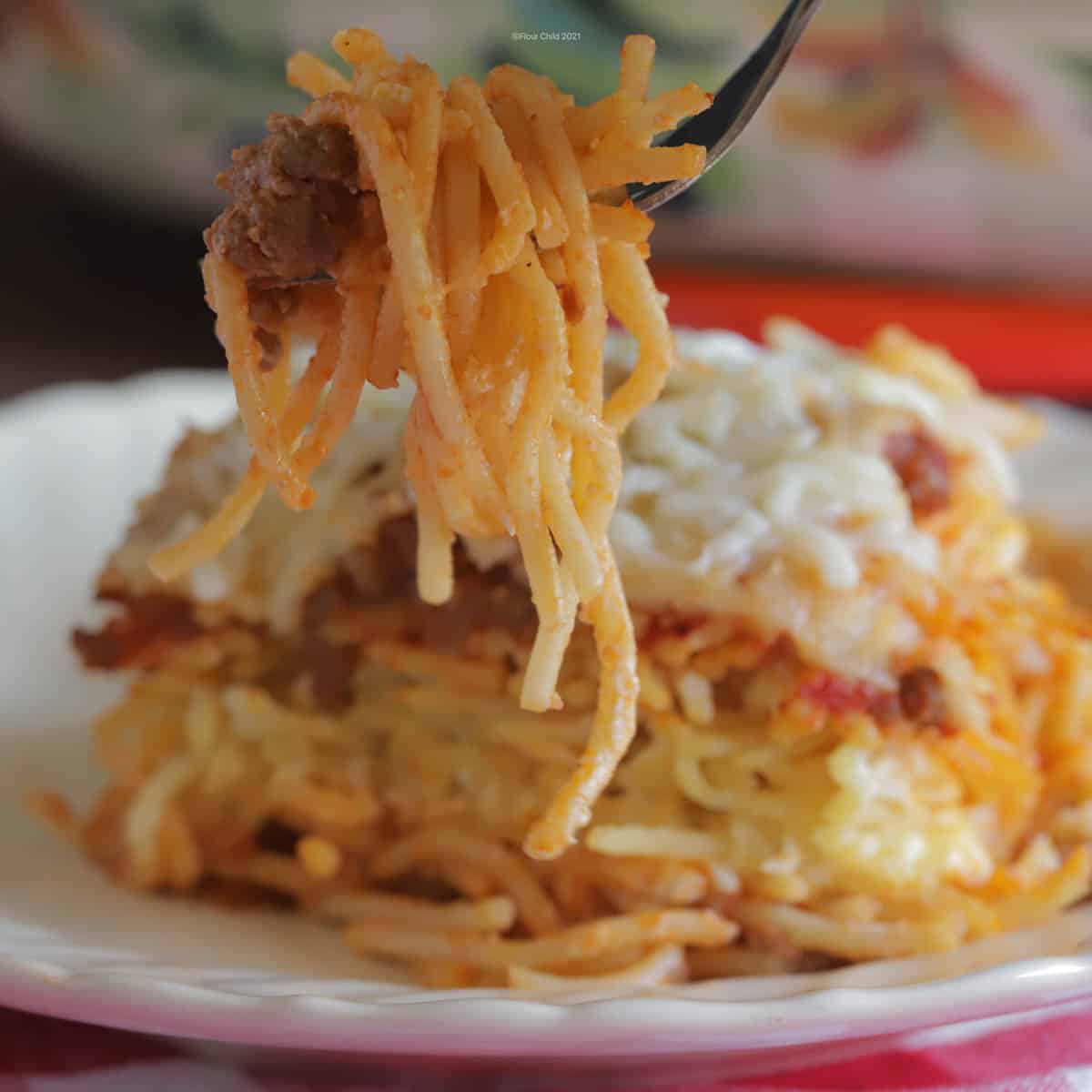 Fork scooping some spaghetti from a slice of baked spaghetti on a plate