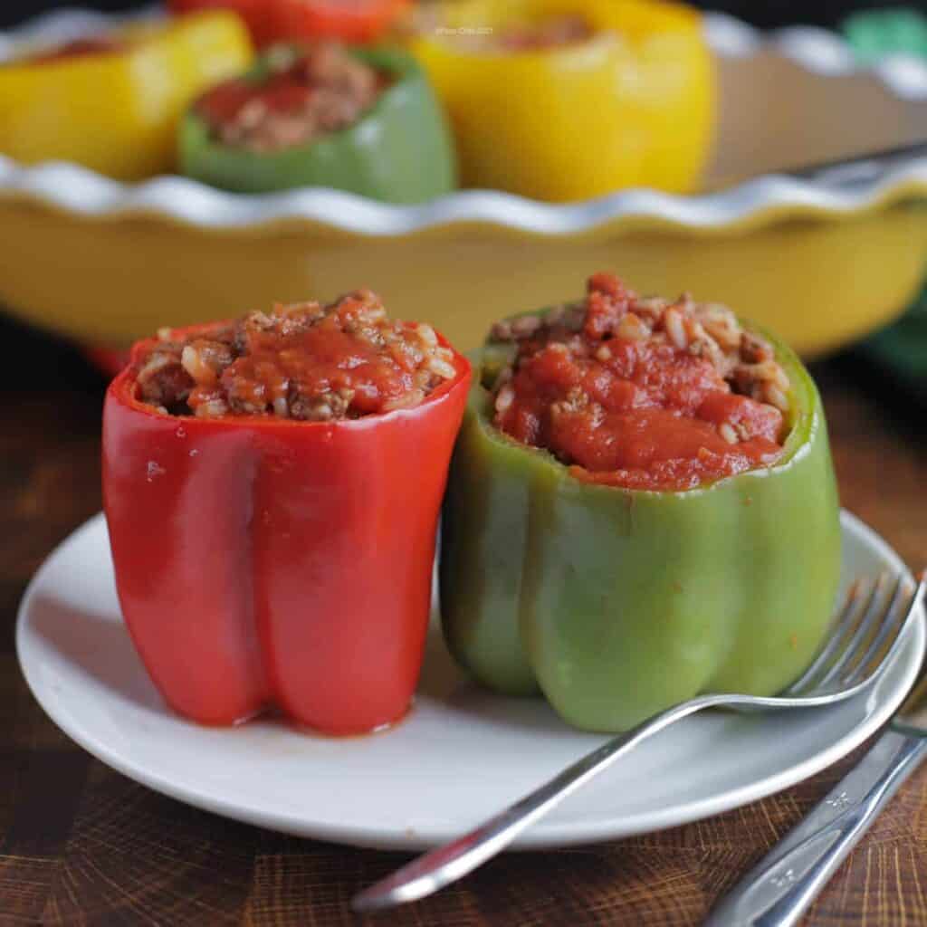 A red and a green stuffed bell pepper on a white plate next to a fork