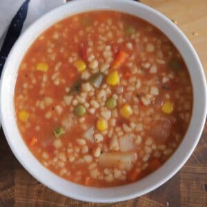 A close up image of vegetable barley soup in a white bowl