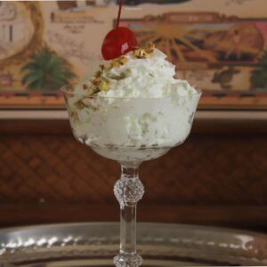 A dessert dish filled with Watergate salad, topped with whipped topping, with pistachios and a cherry on top.