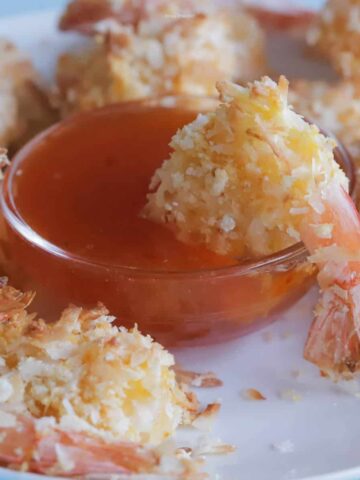 Coconut shrimp on a plate, with a small bowl of apricot dipping sauce that has a shrimp dipped into it.