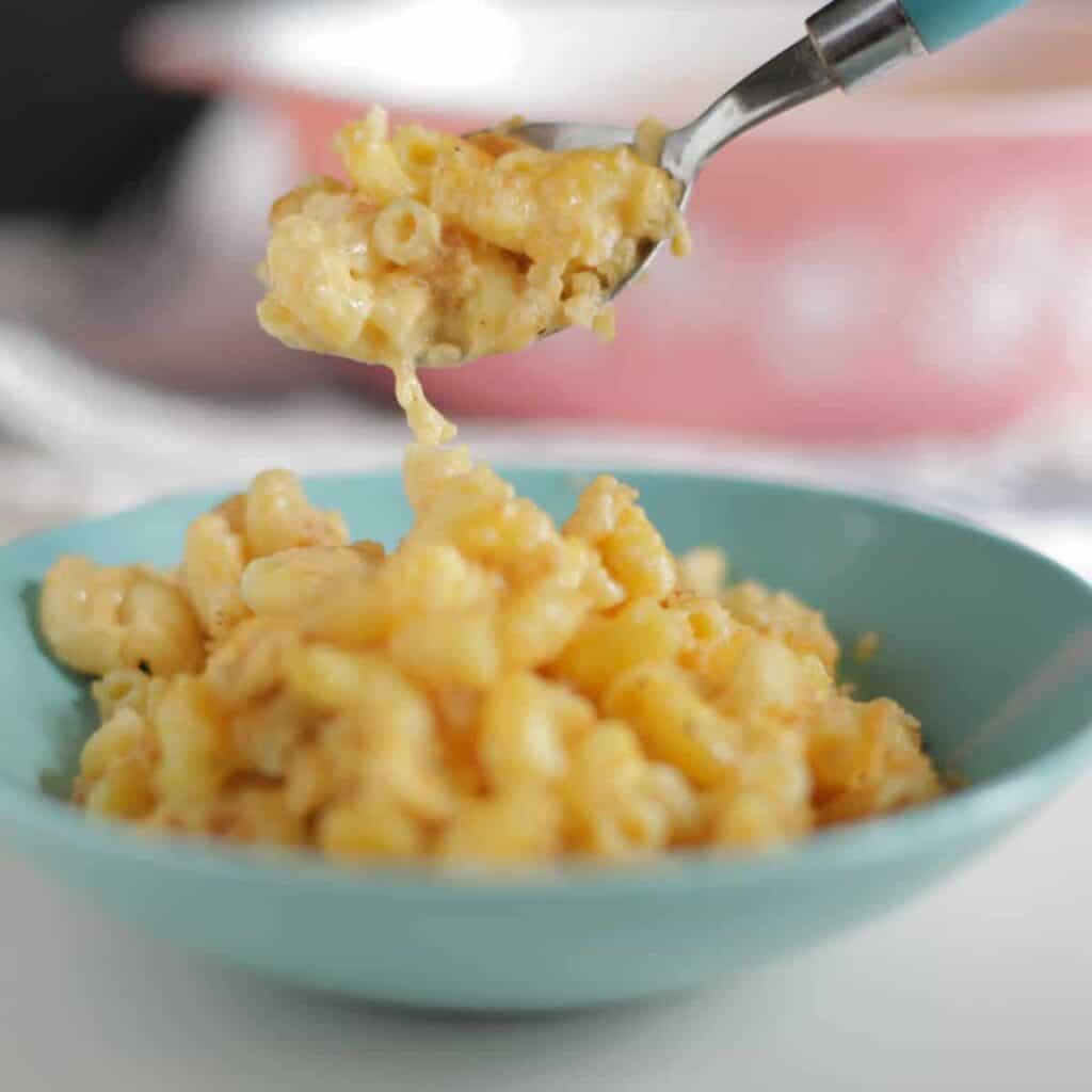 A spoonful of macaroni and cheese being taken from a blue bowl.