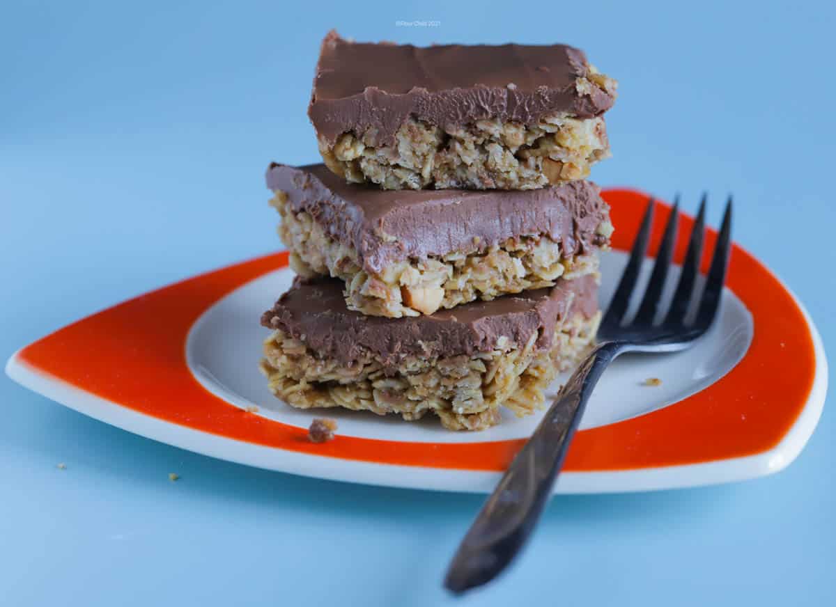 A stack of 3 oatmeal squares on an orange plate with a fork sitting next to them