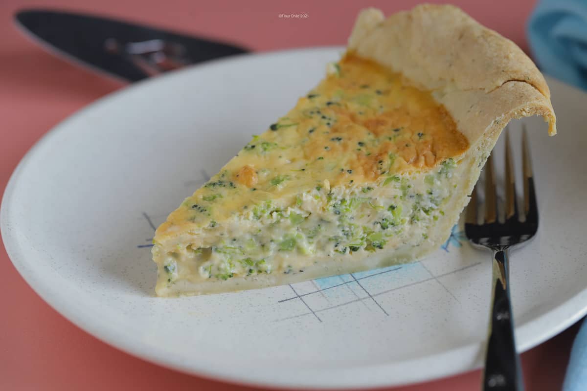 A slice of broccoli and cheddar jack cheese quiche on a plate