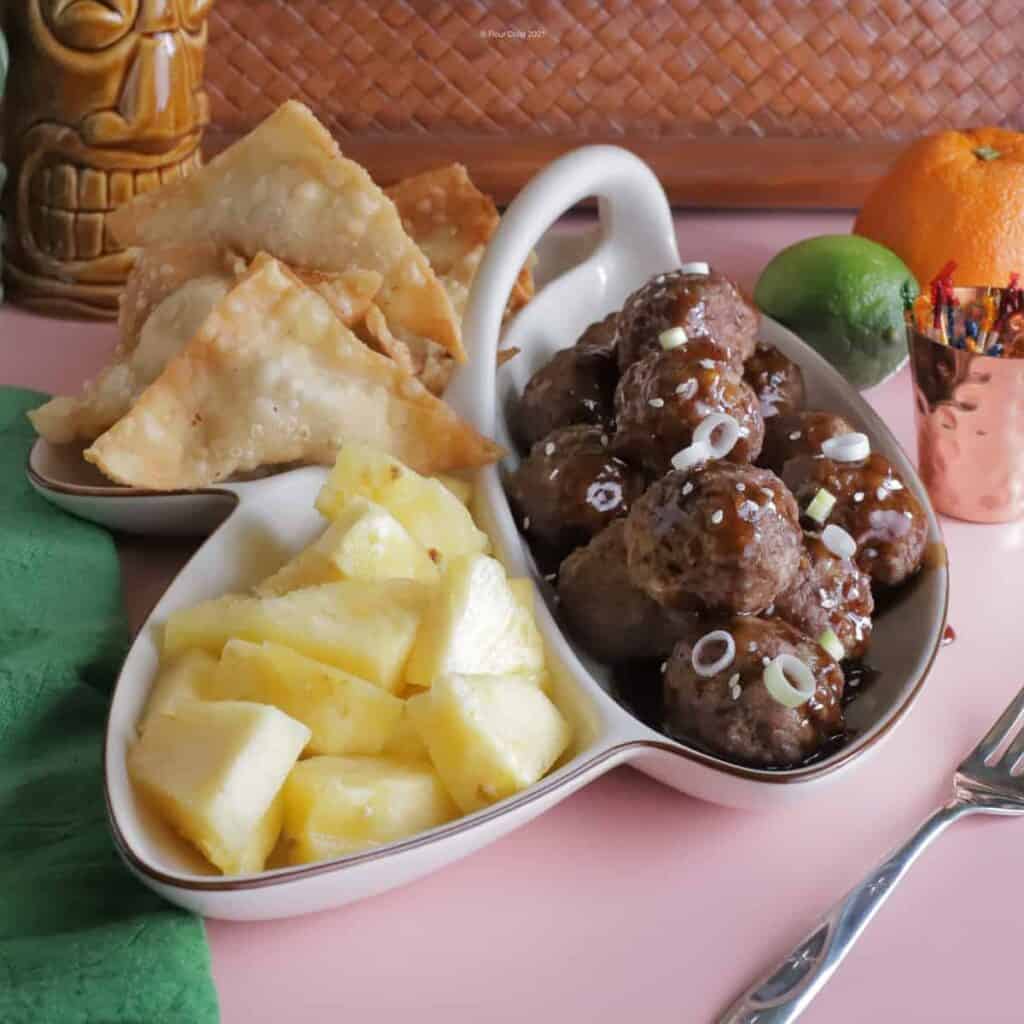 Divided 3-way pupu platter tray with crab rangoon, teriyaki meatballs, and fresh pineapple chunks.