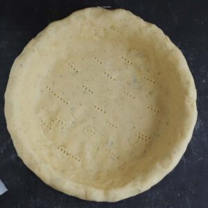 An empty quiche crust in a pie plate.