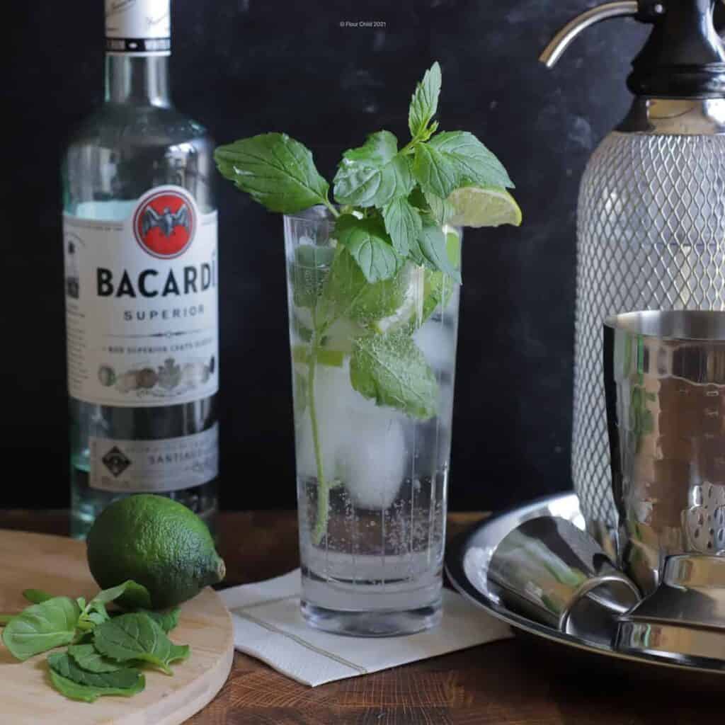 Mojito cocktail in a highball glass chunks of lime and mint leaves.